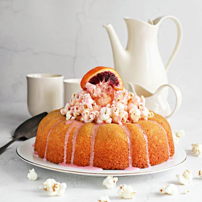 This blood orange cake makes great use of a seasonal citrus treat - and topped with crunchy popcorn and drizzled with blood orange glaze for a sweet and crunchy texture. Blood oranges have distinctly dark colored flesh compared to regular navel oranges and their flavor is more tart and a touch more bitter but with notes of raspberry. The unique taste and appearance makes them highly sought after during their season from early winter to early spring. Mixing the blood red juice of these oranges with powdered sugar creates the pink tone of the glaze. But you can still get the same (or close!) flavor even when the fruit is no longer in season, by using bottled blood orange juice. After all, this cake is too good to restrict to just one season! We like baking it in a bundt pan because the center column of the pan helps distribute the oven heat evenly and results in a perfectly baked cake. We also take advantage of that center hole to fill with popcorn before glazing because we love a little crunch in our desserts. When the glaze firms up on top of the popcorn, it creates a candy-like shell that you'll want more of. But, hey, you can always double the glaze recipe and just pour it over a separate bowl of popcorn.